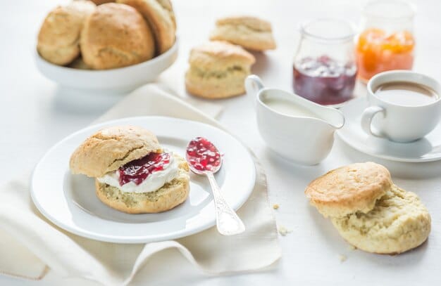 An elegantly set table featuring a selection of English tea sandwiches, scones with clotted cream and jam, and a pot of English breakfast tea, evoking a traditional afternoon tea party in a garden setting.
