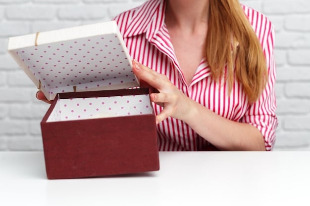 A close-up shot of a Book of the Month box being opened, revealing a newly released hardcover book. The box also contains a bookmark and a note from the editor. The focus is on the tactile experience of receiving a physical book.