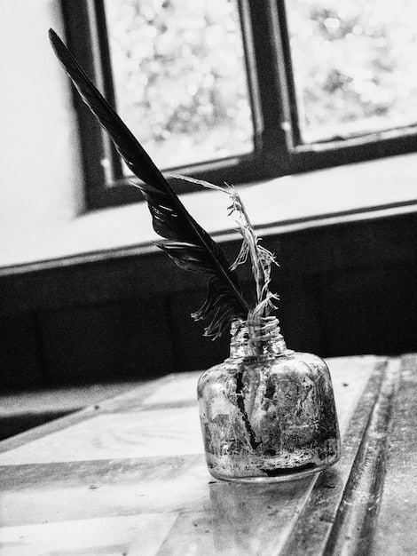 A black and white photograph of Jane Austen's writing desk, with a quill pen and inkwell on top. The image is taken inside a small, elegant room with historical artifacts surrounding it.