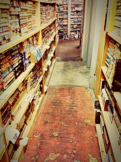 Display in a cluttered thrift store with shelves filled with used books of different sizes and colors. Shoppers were browsing the selections.