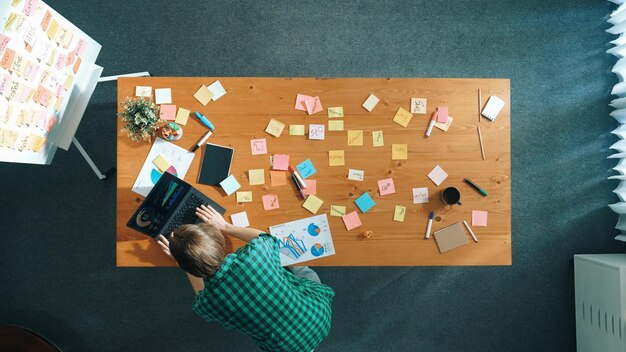 A person sitting at a desk with a laptop, surrounded by sticky notes filled with ideas and plot points. The scene conveys a sense of brainstorming and creative organization.