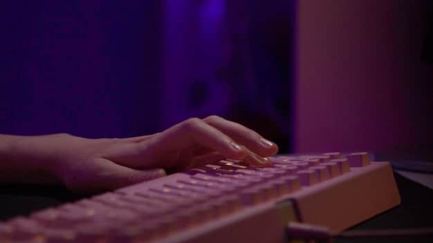 A close-up shot of a writer's hands hovering over a keyboard, with a focused expression on their face. The dimly lit environment emphasizes the mystery and suspense associated with thriller writing.