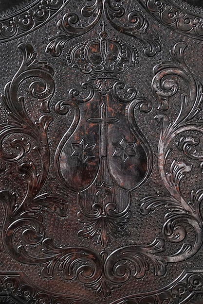 A close-up of an old, leather-bound book with ornate gothic lettering on the cover. The book is open, and the pages are filled with handwritten text in a dark ink. A raven's feather rests on the open pages.