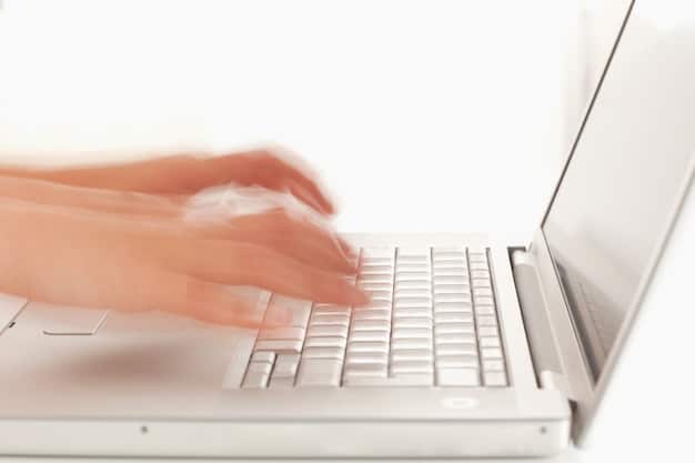 A close-up shot of a person's hands typing on a laptop, with a partially visible book cover on the side, suggesting they are writing a book review. The lighting is soft, and the background is blurred, creating a focused and productive atmosphere.