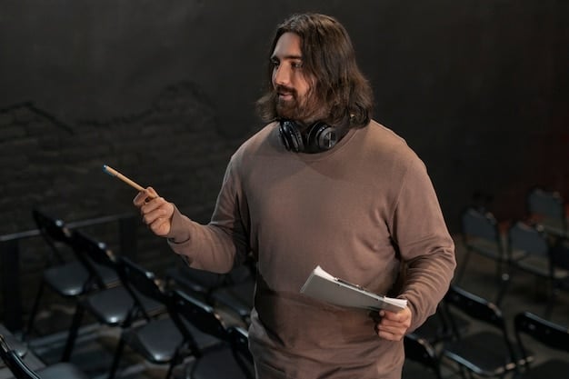 Close-up of a theater critic taking notes during a performance. The critic is middle-aged, wearing glasses, and has a serious expression, suggesting focused attention. The stage is visible in the background, blurred but showing actors in costume.