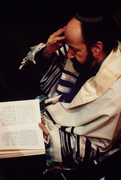 A close-up shot of a theater critic taking notes during an improvisational performance. The critic's expression is thoughtful and engaged, suggesting a careful observation of the unfolding scene.